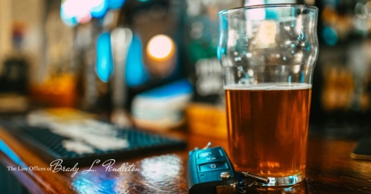 Close up image depicting a partially consumed pint of beer next to a set of car keys on the bar counter, illustrating a drunk driving concept
